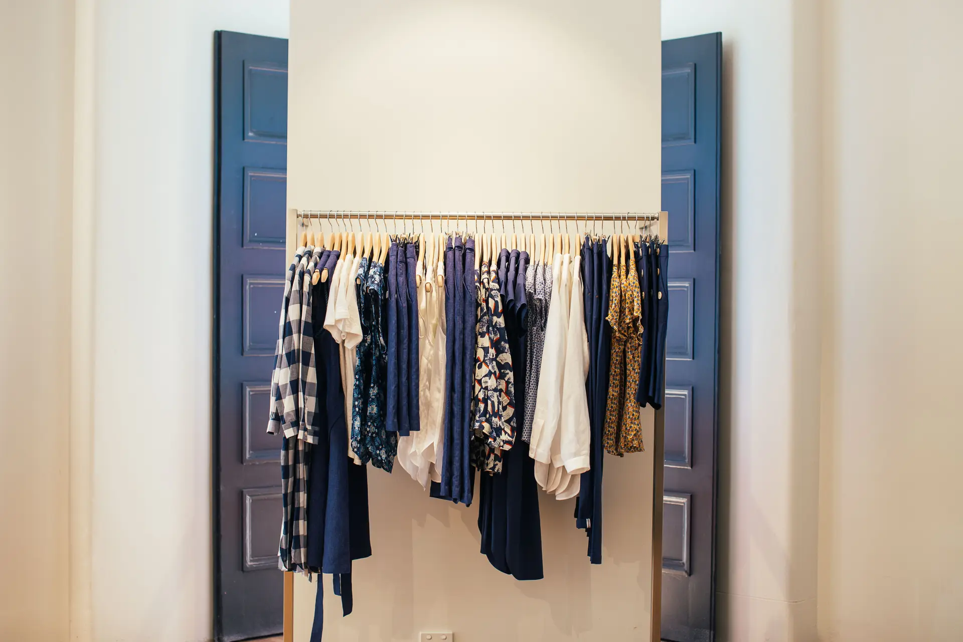Clothing rack in a white shop interior with blue doors